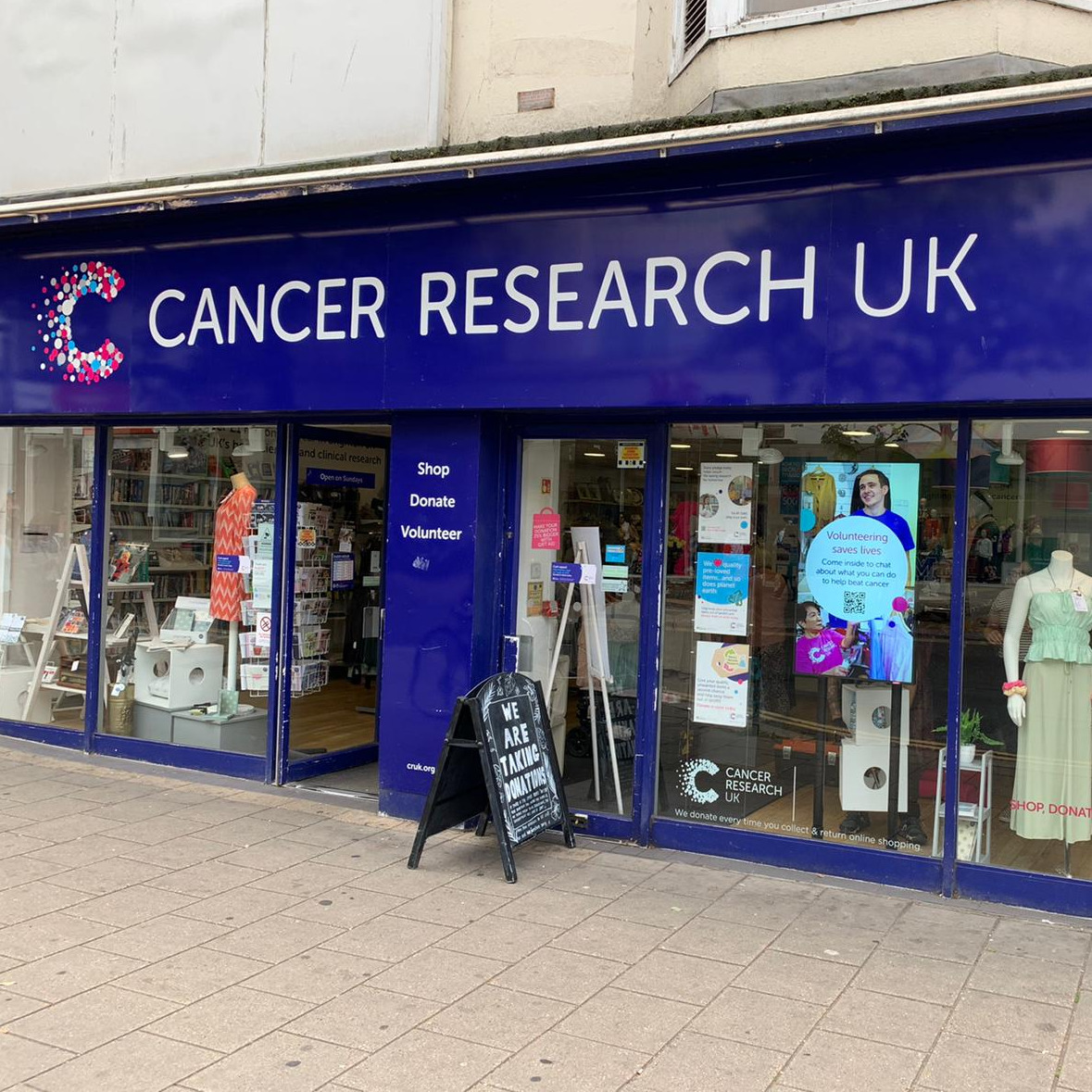 cancer research UK screen in shop window advertising volunteering