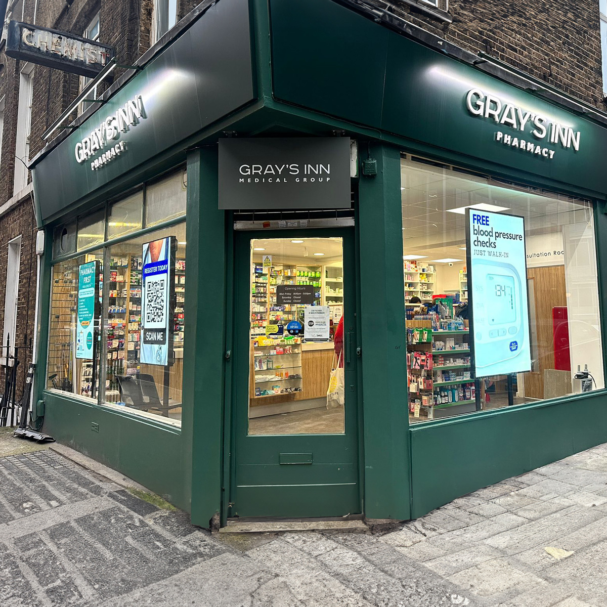 grays inn pharmacy with three digital window adverts promoting free blood pressure checks and registering to them with a qr code